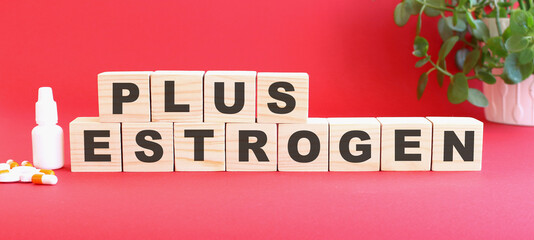 The words PLUS ESTROGEN is made of wooden cubes on a red background with medical drugs. Medical concept.