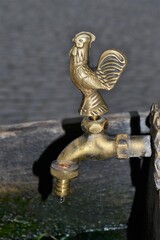 Water faucet or tap with a bronze figure of a rooster. Details of the wooden well in Kazimierz Dolny, Poland. An artistic tap at the well