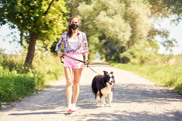 Naklejka na ściany i meble Picture of adult woman strolling with her pet and wearing a mask