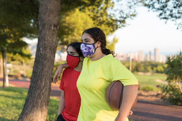Young man and woman walk to the court with a basketball and protective mask.