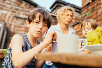 Happy middle age blond mother carring her children. Mature woman with sons eating fruits and dessert at terrace over brick wall on backyard.