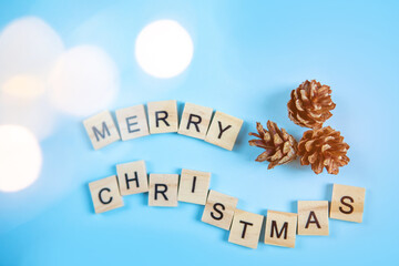 Fototapeta na wymiar Wooden letters with the inscription merry christmas with fir cones and on a blue background