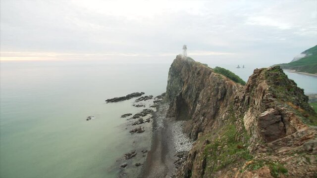 Timelapse of a high cliff above the sea and the path leading to the lighthouse on its top. Light morning fog. Far East of Russia