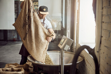 Male worker weighing green coffee beans at factory