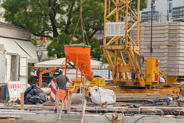 Mann weist kran mit betonKübel auf der Baustelle ein