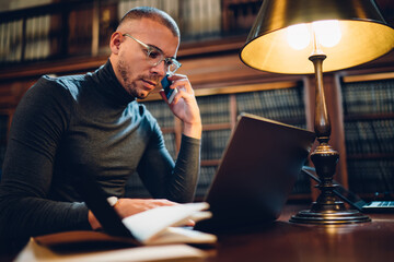 Intellectual student in bifocal eyewear making service conversation for consultancy about banking operation on laptop solving problem with online payment of webinar tutorial, education and technology