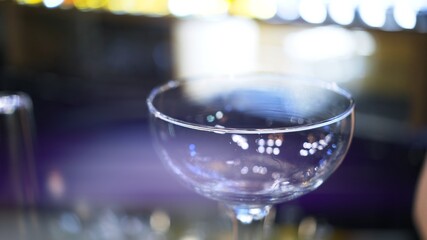 Empty cocktail glass on a bar counter, close up lens flare. Cocktail glass focused shot inside on blurred background, making cocktail concept