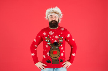 Christmas party time. cold weather fashion for men. happy new year. bearded man on red wall. funny man with beard in knitted sweater. pazzled hipster ready for xmas party. winter holiday celebration