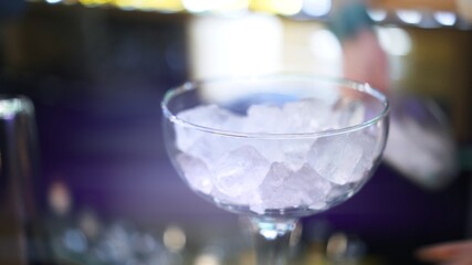 Cocktail glass with ice on a bar counter, close up lens flare. Cocktail glass focused shot on blurred background, macro shot making cocktail concept