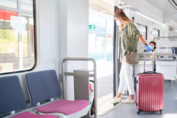 Young woman wearing face mask and gloves, carrying a suitcase getting off the train. New normal...