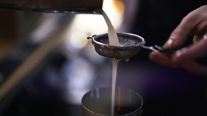 Bartender pouring alcohol through a strainer, close up shot, lens flare. Cocktail pouring from stainless steel cup, cocktail making process, blurry background