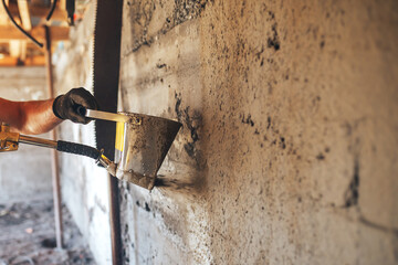 Man plastering a wall with mortar using a hopper bucket.