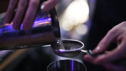Bartender pouring alcohol through a strainer, close up shot, lens flare. Cocktail pouring from stainless steel cup, cocktail making process, blurry background