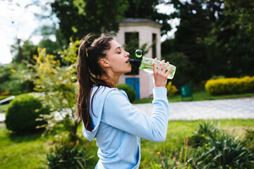 Young woman in a sporting suit drinks from a bottle after a workout