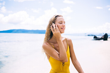 Carefree female swimmer listening noise of sea from shell mollusk enjoying tranquility time at beach coastline on Cayman island, charming woman feeling serene calmness during summer resort vacations