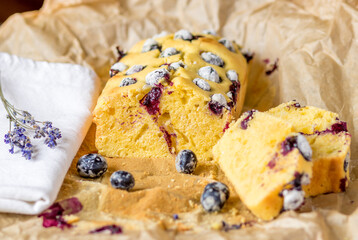 Selective focus to the soft yogurt plumcake with blueberries on baking paper at the table.