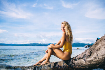 Young blonde sitting on dead tree and looking at camera on beach
