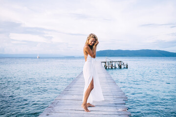 Happy shapely female in light dress standing on pier