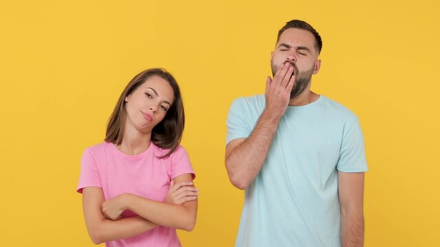 Young sad exhausted boring couple friends bearded man woman 20s in basic t-shirts isolated on yellow background studio. People emotions lifestyle concept. Look at camera wait folded hands sigh suspire