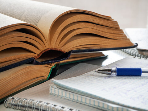 Two old thick books are on the table, one on top of the other. Nearby are notebooks with notes. Books and notebooks are open. The pen is on the notebooks. Background for education and libraries.