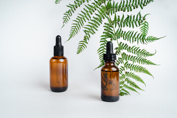 Dark glass bottles stand on wooden cuts, next to  branch. Monochrome photography trend. Isolate on white background. Place for text. Bottle of Spa essential oil for aromatherapy 