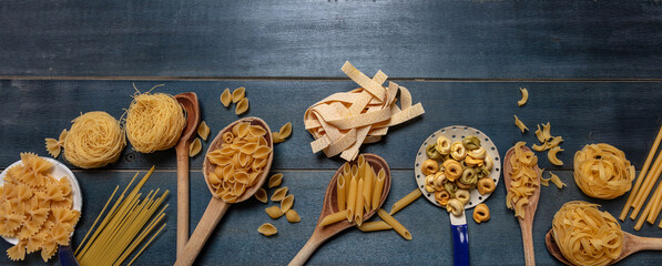 Fototapeta na wymiar Pasta assortment on blue background, top view. Cooking italian cuisine concept