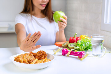 Close up of young Asian woman using hand push out her favourite fried chicken, french fries and choose green apple, vegetables for good health. Woman on dieting concept. Close up