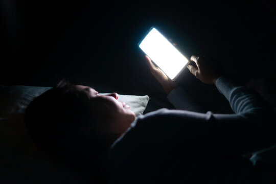 Young beautiful woman in bed using smartphone late at night in dark bedroom. Mobile phone, internet addiction, Insomnia  concept