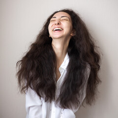 Portrait of young woman with brunette curly hair in a white shirt over simple background.