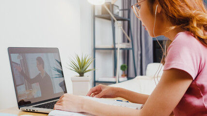 Back view of Young Asia teen girl student wears headphones distance learning lesson with online...