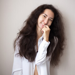 Portrait of young woman with brunette curly hair in a white shirt over simple background.