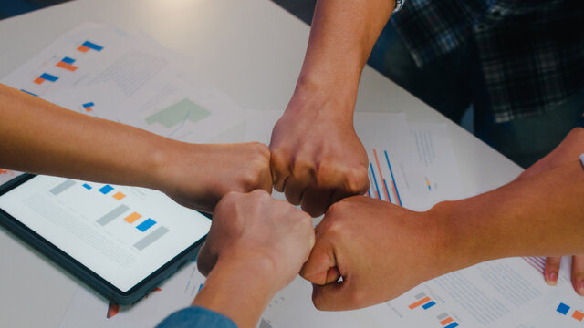 Asia businessmen and businesswomen colleagues fist bumping celebrating successful teamwork friendly happy motivated coworker excited by good work result congratulating at meeting room in home office.
