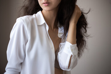 Portrait of young woman with brunette curly hair in a white shirt over simple background.