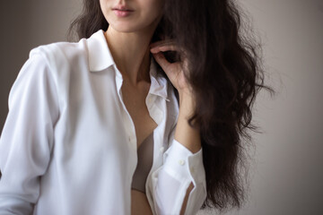 Portrait of young woman with brunette curly hair in a white shirt over simple background.