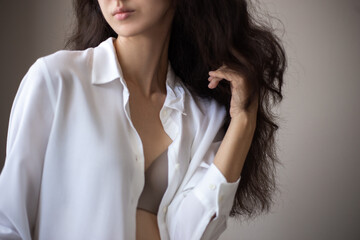 Portrait of young woman with brunette curly hair in a white shirt over simple background.