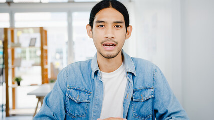 Fototapeta premium Asia businessman social distancing in new normal situation for virus prevention looking at camera presentation to colleague about plan in video call while work in office. Lifestyle after corona virus.