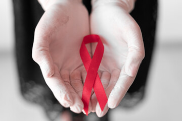 medicine concept - female hands in medical gloves holding red AIDS awareness ribbon.