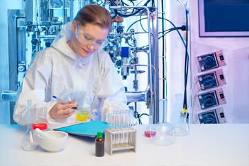 Fermentation reactions in pharmacology. The girl is sitting at a table with chemical dishes. Girl on the background of a laboratory bioreactor. Microbiological examination.