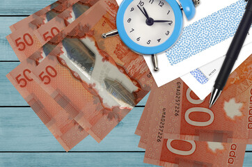 50 Canadian dollars bills and alarm clock with pen and envelopes. Tax season concept, payment...