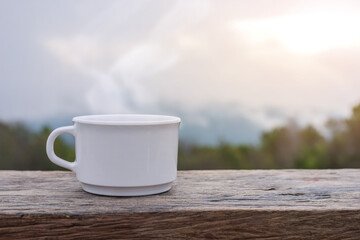 coffee cup on wooden table with morning foggy background.