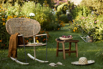Stylish composition of countryside garden with design rattan armchair, wooden bench, plaid, food,...