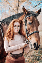 Fototapeta premium Beautiful red haired woman with horse posing outdoors on autumn background