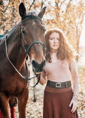 Obraz premium Beautiful red haired woman with horse posing outdoors on autumn background