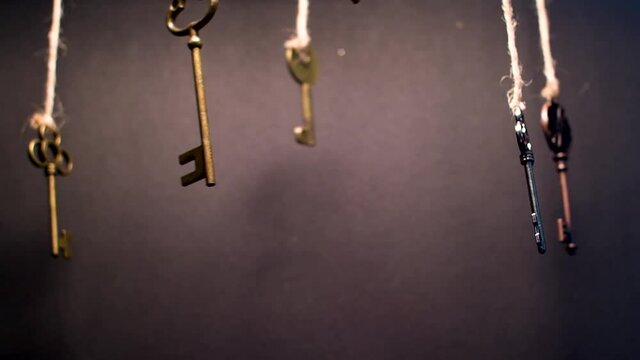 A lot of different old keys from different locks, hanging from the top on strings. Finding the right key, encryption, concept. Retro vintage brass keys on a dark background, low depth of field