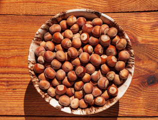 Hazelnuts in porcelain bowl on rustic wooden background. Raw fresh homegrowing nuts from house garden top view natural shadow. Organic dietary fiber, protein, vitamins source, healthy weight loss diet