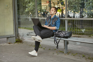 White man with laptop on bus stop.