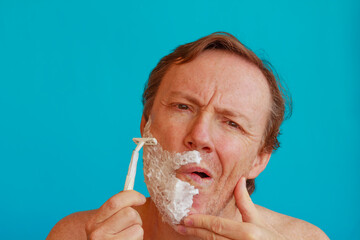 a man shaving his beard with  razor -blade /A man tilts his face and stretches the skin with your hand to shave his beard with  razor-blade