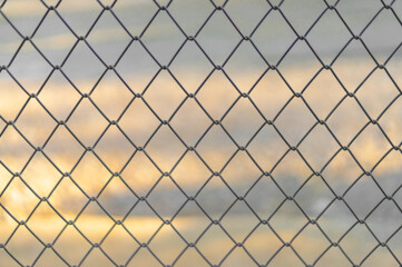 The blurred background of a gray iron door crossed into equally spaced rhombus panels. The backdrop of the orange sky as the sunsets. Feeling safe and secure. Idea for grid wallpaper with copy space.