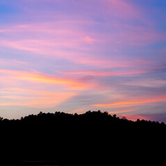 A photograph of clouds pattern in the twilight colored sky in the evening. The bellow edge of the image is a black large mountain. Feeling calm, relax, and romantic. There is a copy space on top.