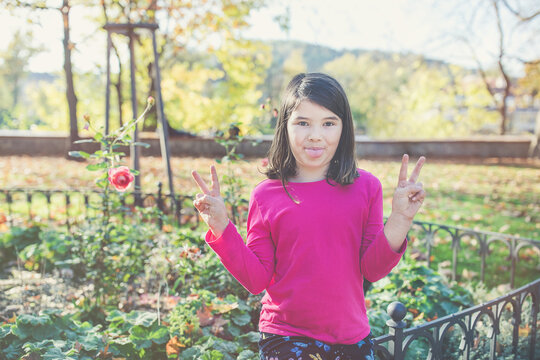 Happy mixed race Japanese girl in autumn park, looking camera showing tongue and v-sign with both hands. Sunny day, copy space, funtime concept